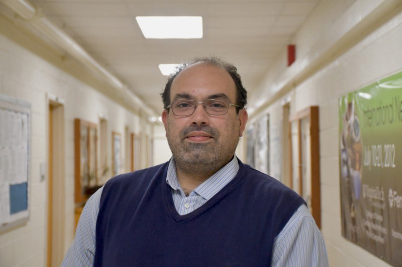 Camillo Mariani, a scientist at Virginia Tech, poses for a photograph in a hallway. He is wearing a vest over a dress shirt.