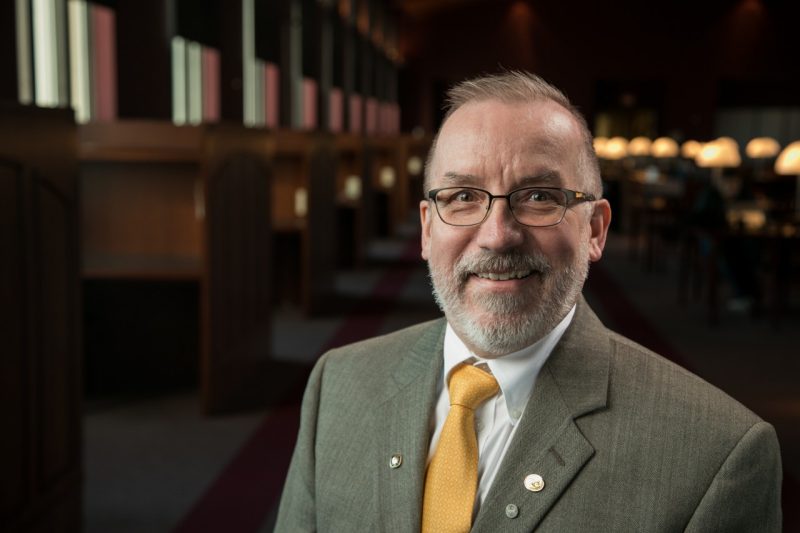 Leo Piilonen , a professor of physics, wears a suit and tie as he poses in the Torgersen Hall Bridge.