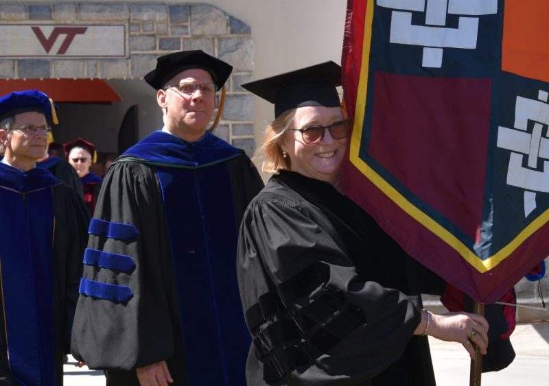 Sharon Stidham, in cap and gown, carries the Graduate School banner in procession