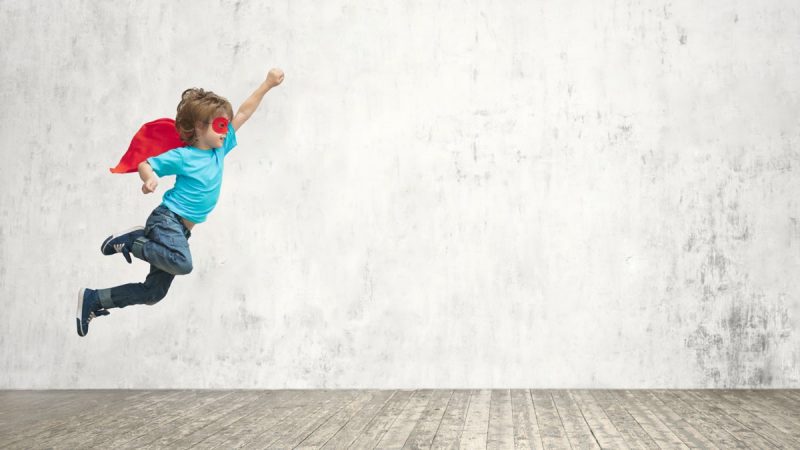 Kid wearing a mask and cape jumping in an empty room