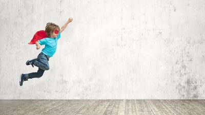 Kid wearing a mask and cape jumping in an empty room