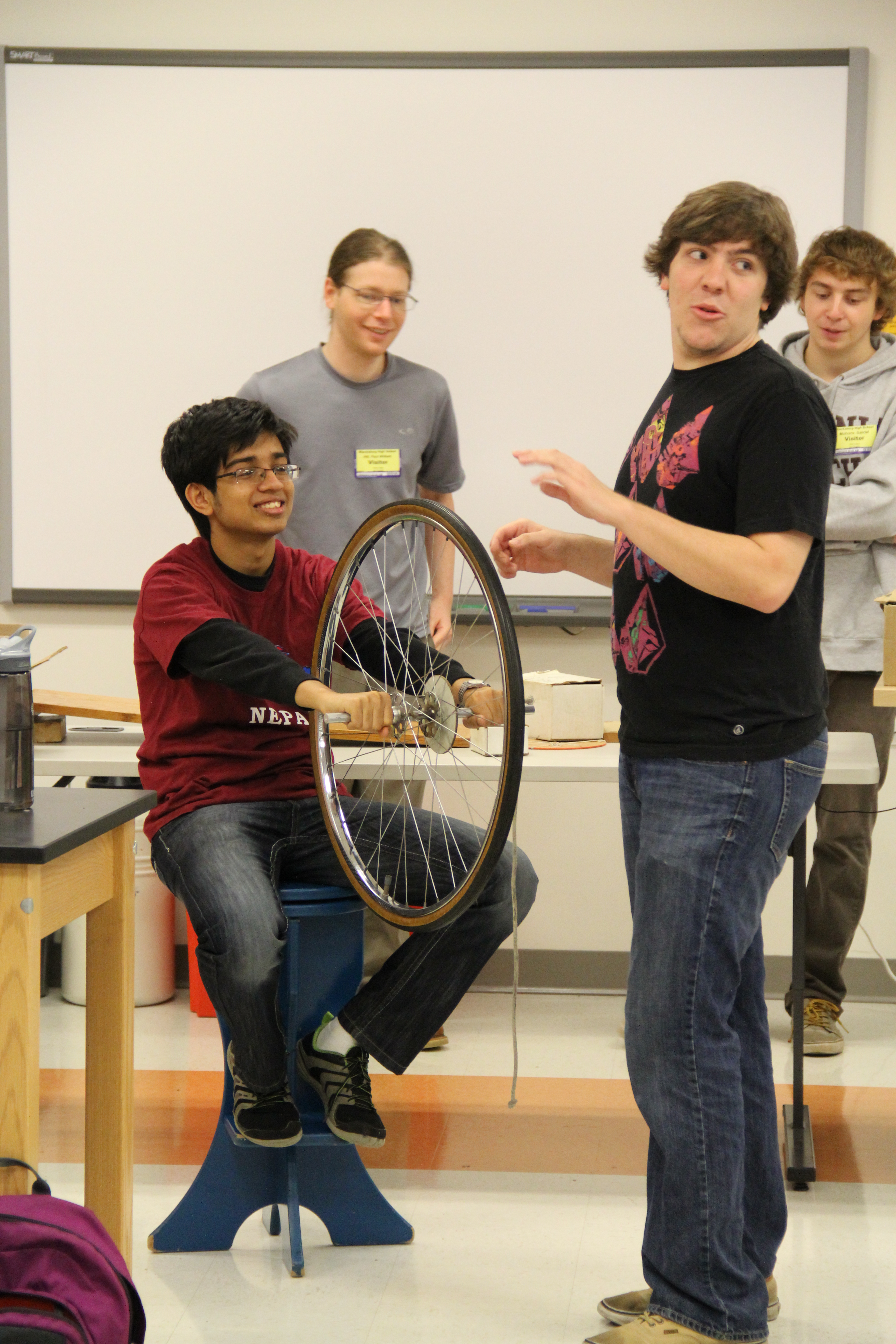 Outreach students Paul, Will, and Gabe showing a Blacksburg High School student how a bicycle wheel transfers angular momentum when turned