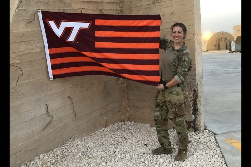 Capt. Kimberly Markovcy Veal holds a Hokie flag against a concrete wall while deployed to southeast Asia.