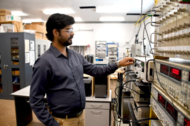Physics doctoral student Adbhut Gupta in the lab of Jean Heremans at Robeson Hall. Wearing a dark shirt and trousers, Gupta is working with machinery that is used to track electrons.