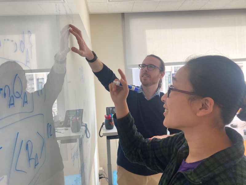 Two mathematicians working on math problems at a whiteboard.